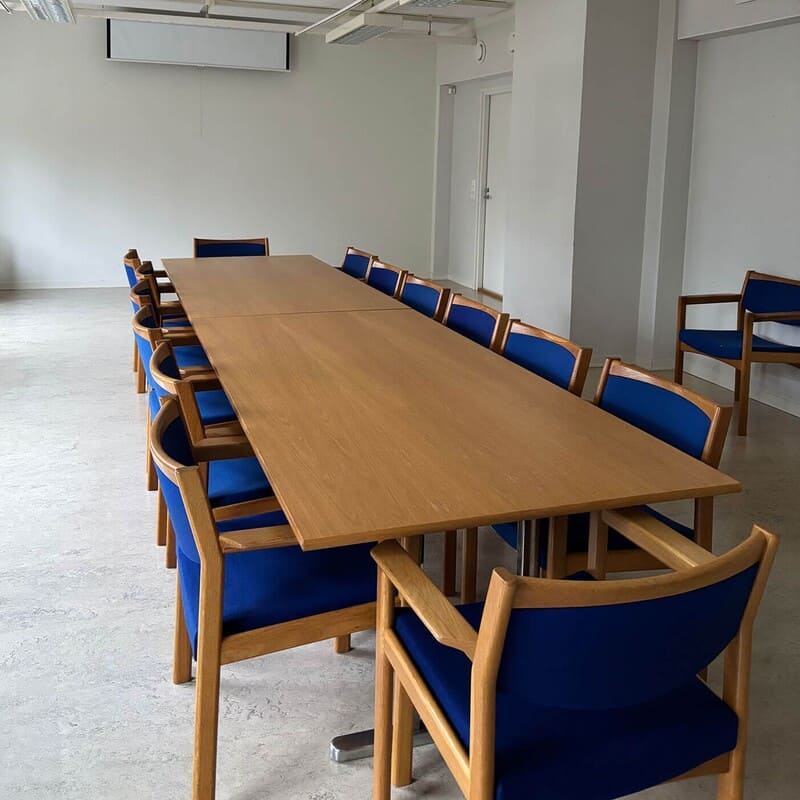 Kokoussali pitkällä puupöydällä ja sinisillä tuoleilla 30 hengen tilaisuuksiin